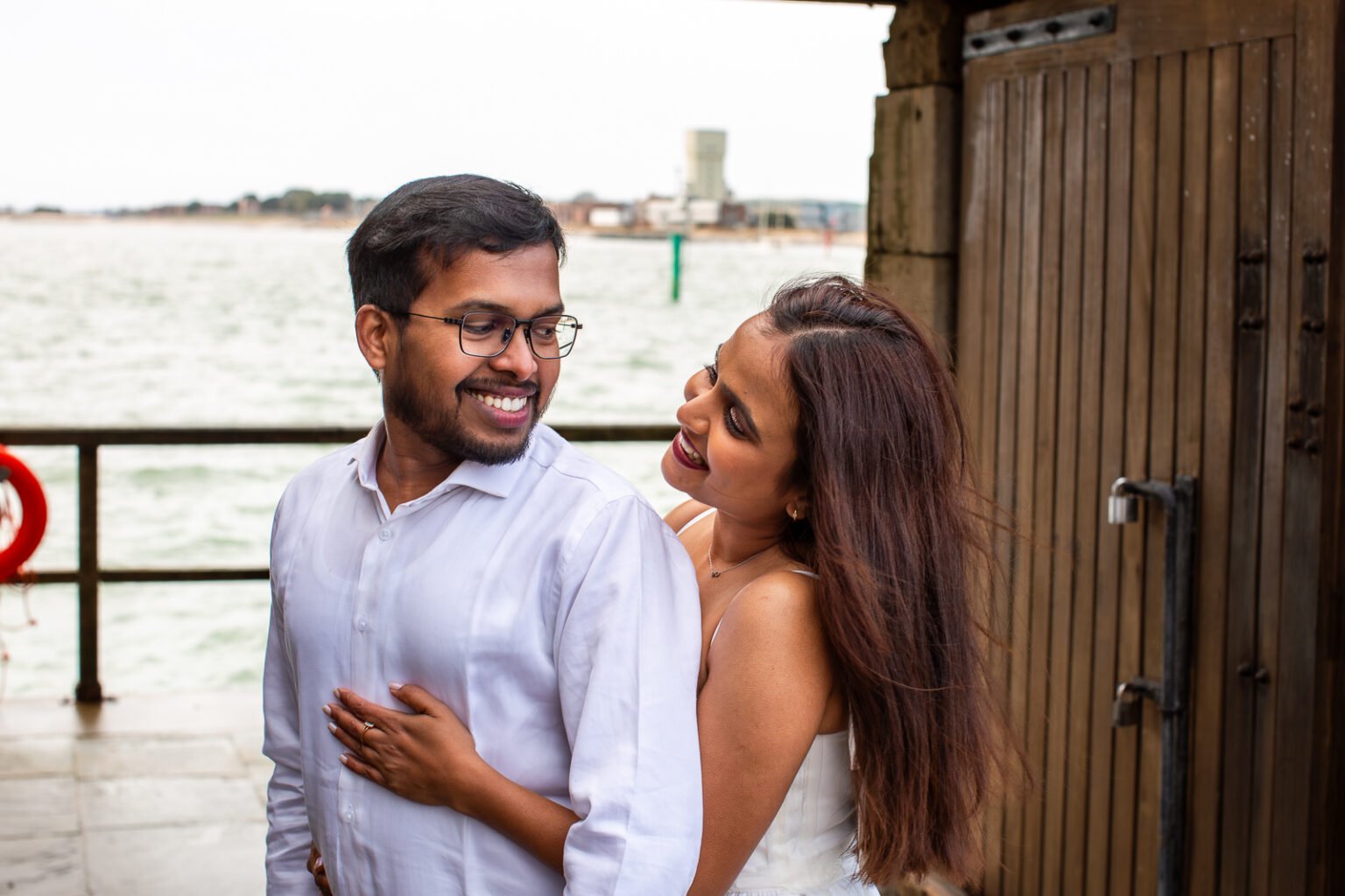 Bride and groom are looking at each other in front of the beach at Old Portsmouth during couple photography session.